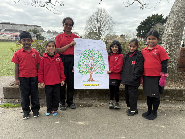 Students stand beside a collaborative fingerprint tree artwork celebrating participation and belonging.