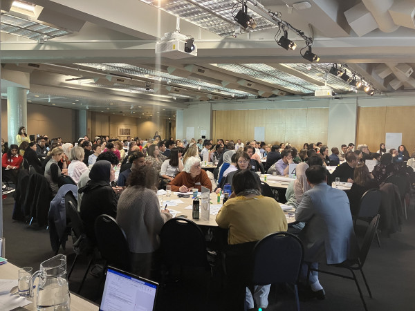 Image of the National Refugee Resettlement Forum 2026 attendees seated around tables in a large room, listening to ideas for improving refugee education.