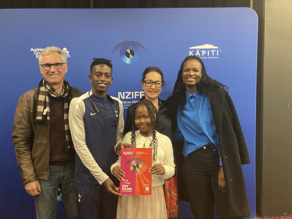 Abdulhakim, Ko Parsons and Qemajl stand together in front of a blue New Zealand International Film Festival backdrop. One person holds a New Zealand International Film Festival programme.