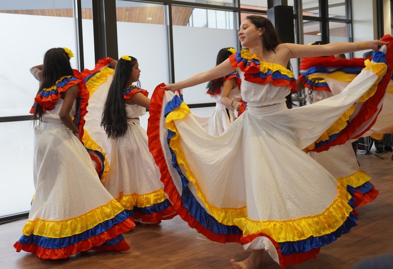 Five Columbian dancers circle the dancefloor in long flowing white dresses hemmed with the colours of their flag at INZ's pōwhiri for refugees